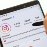 The screen of a smartphone opened in the Instagram profile page where a hand is pointing over the high number of followers.
